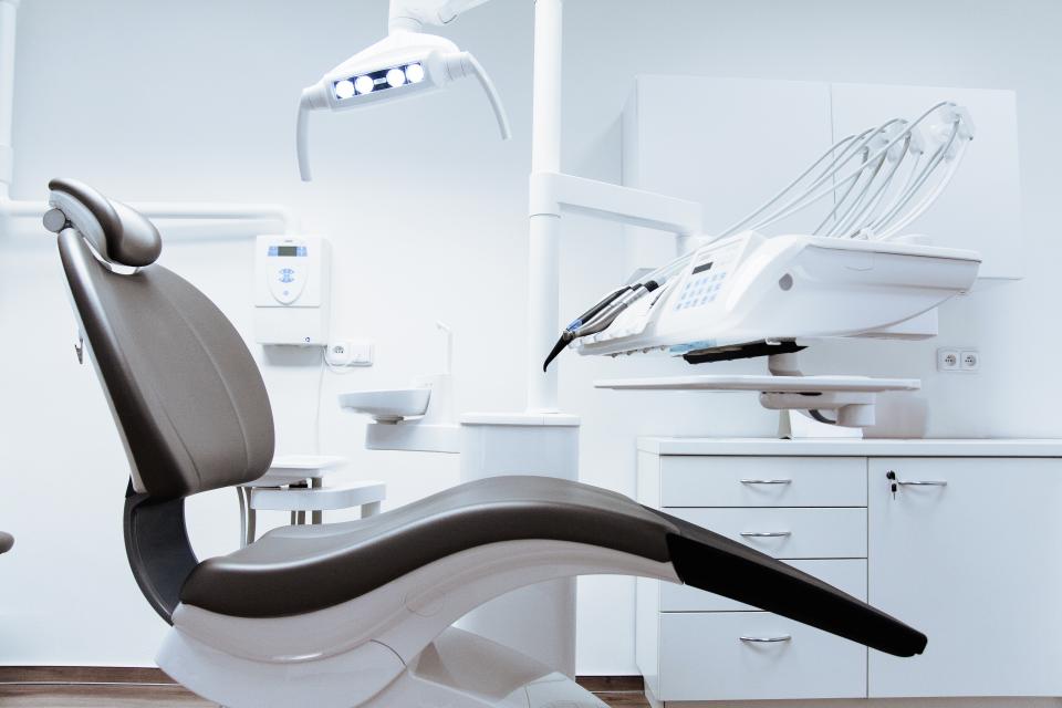 Sillón de dentista y su equipo en una consulta blanca, con el brazo de instrumental y la lámpara sobre el cabezal.